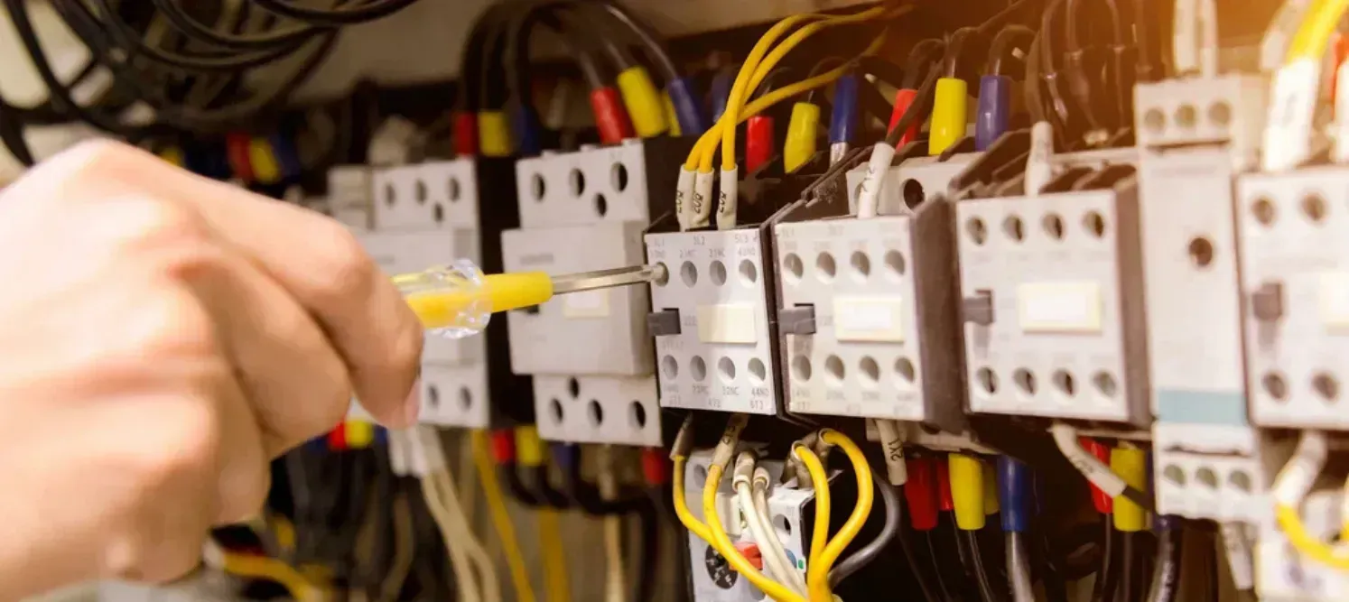 Electrician tightening wire terminals on contactors inside an electrical control panel
