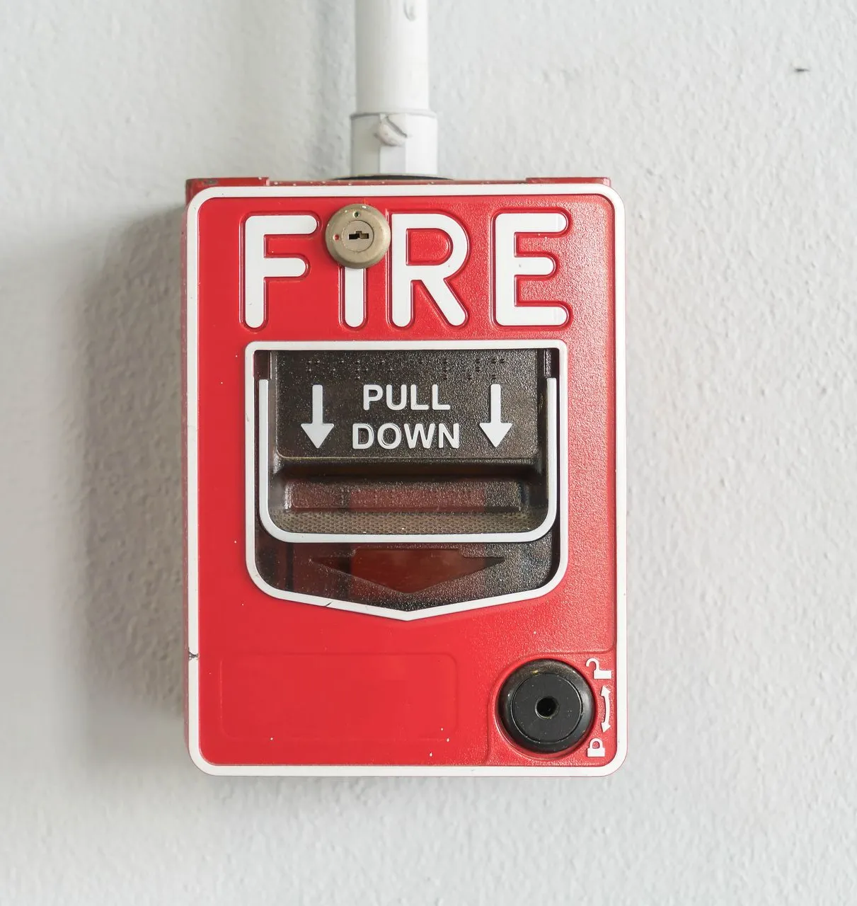 Red “Fire – Pull Down” manual pull station mounted on a white wall