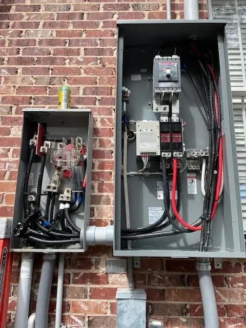 Electrical panel boxes mounted on a brick wall with exposed wiring.