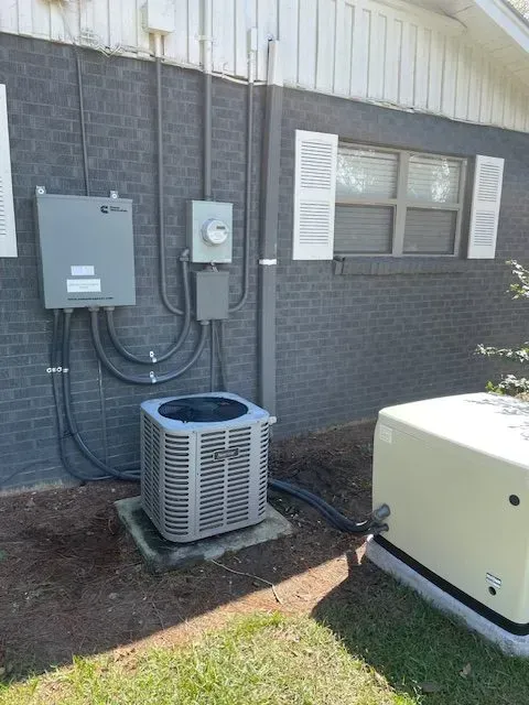 An air conditioning unit and electrical components outside a brick building, alongside a generator.