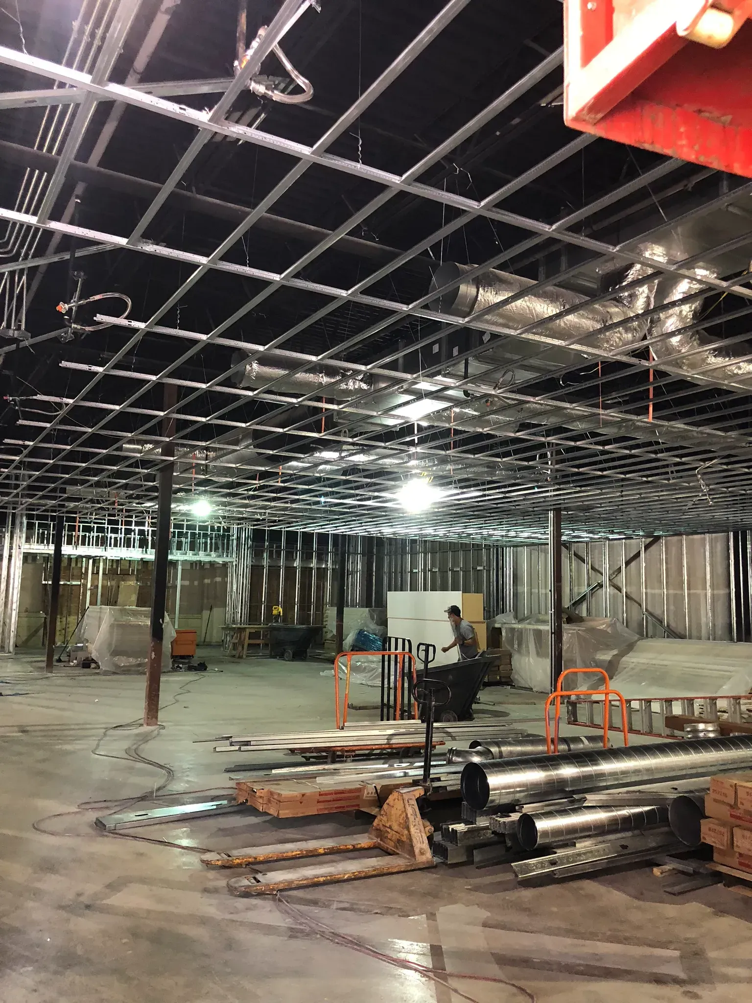 Interior construction site with exposed ceiling grid, walls, and equipment.