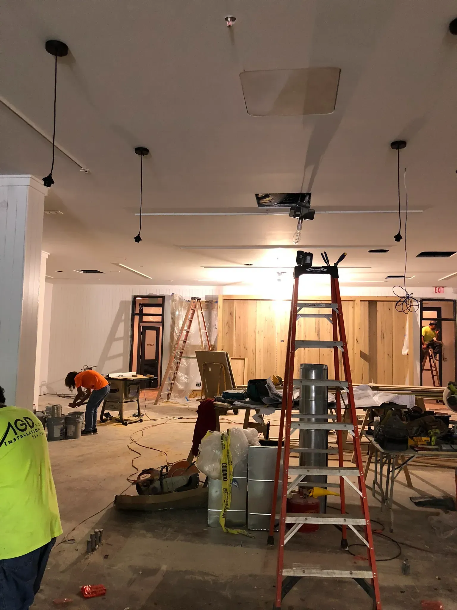 Interior construction site with workers, ladders, and exposed framing.
