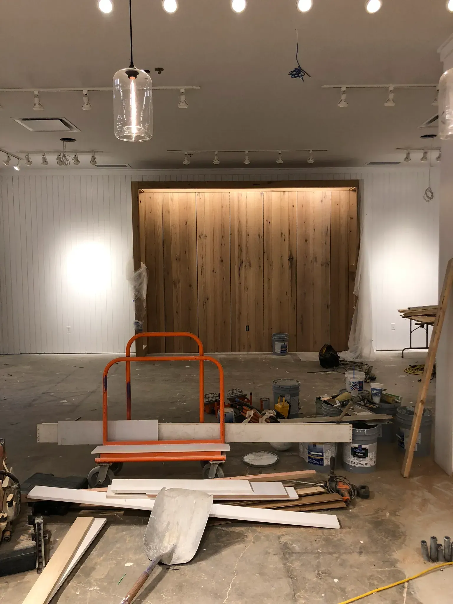 Interior of a retail space under construction. Wooden accent wall, tools, and construction materials are visible.