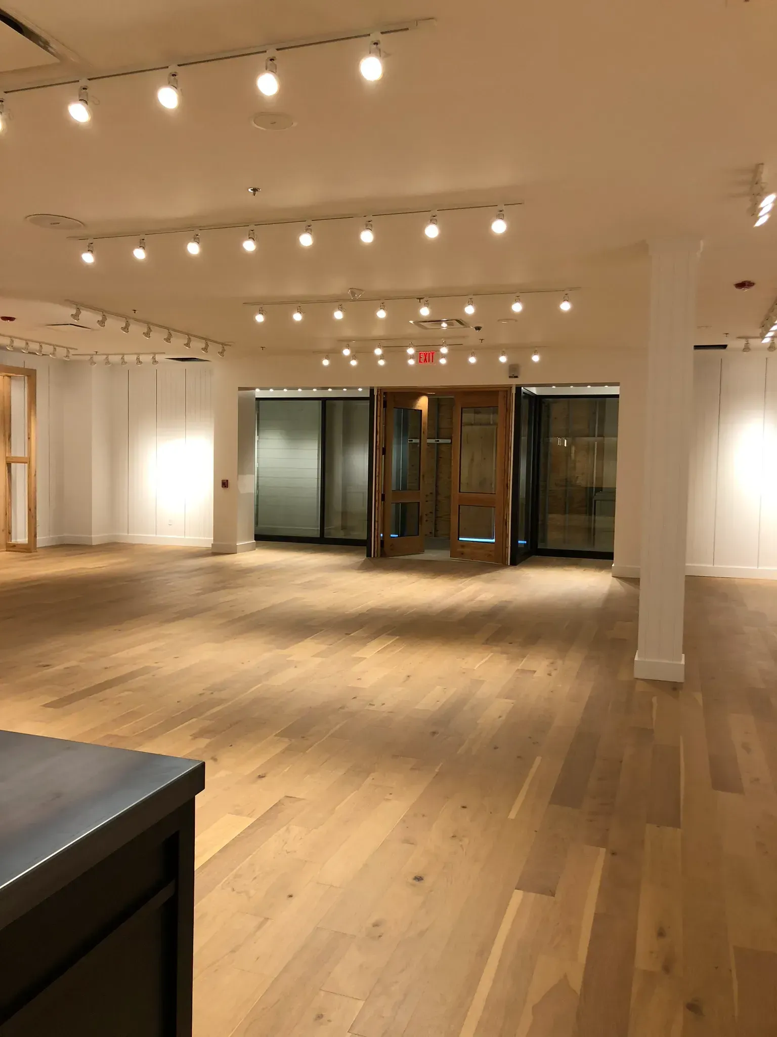 Empty retail space with hardwood floors, white walls, recessed lighting, and wooden doors.