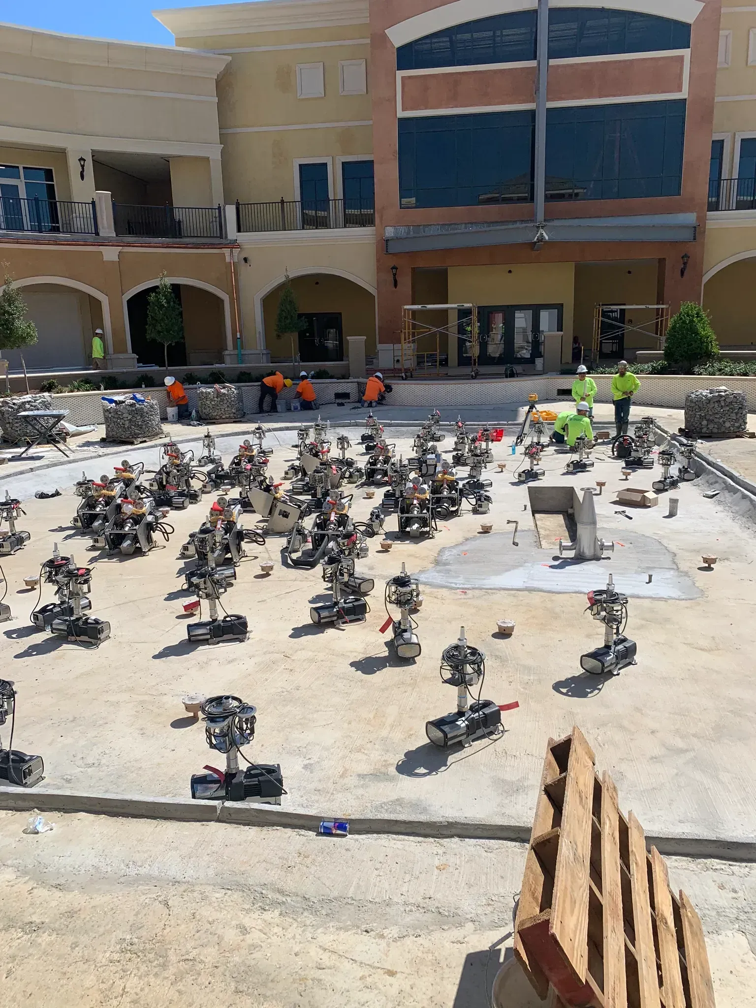 Many small robots on a construction site. Construction workers in orange vests and a building under construction.