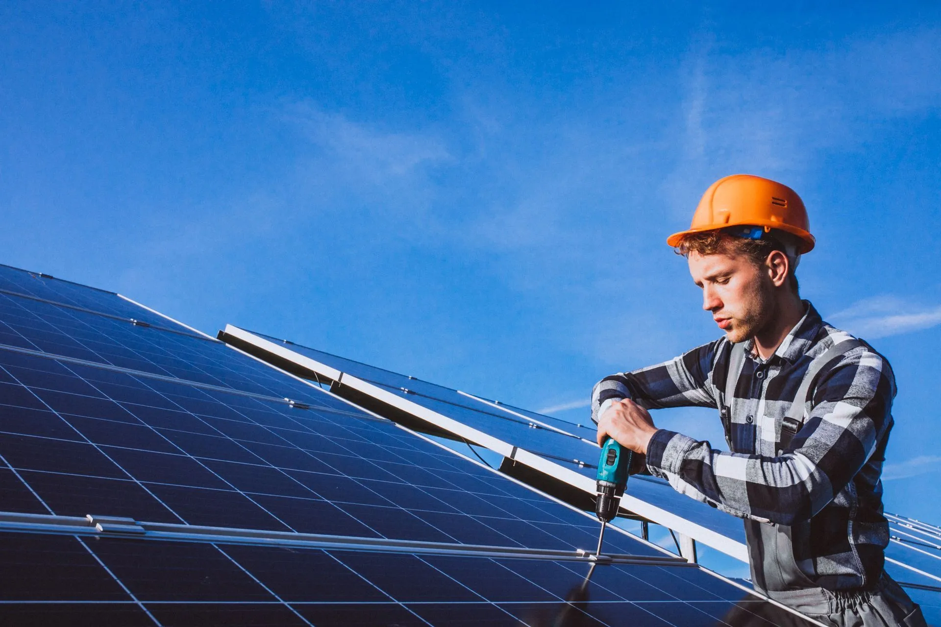 Worker in an orange hard hat fastening a solar panel mount with a drill