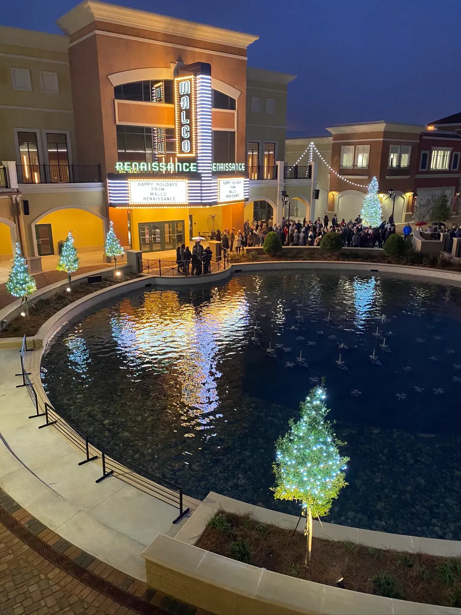 Theater and plaza at dusk. Reflective pond with Christmas tree lights. People gathering by entrance.