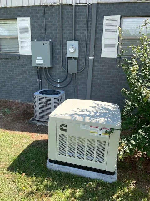 Standby generator next to an AC unit with meter and disconnect boxes on a gray brick wall