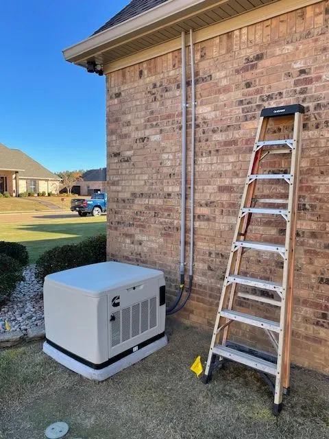 New standby generator beside a brick home with conduit and a ladder against the wall